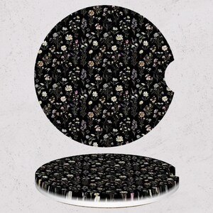 May include: Two car coasters with a black background and a floral pattern. The pattern features small white, pink, and yellow flowers. One coaster is flat, and the other has a curved edge.