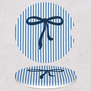 May include: Two blue and white striped car coasters. Each coaster has a navy blue bow design in the center. The coasters are round with a small notch on one side.