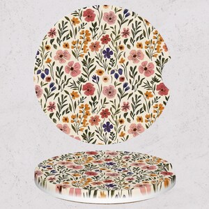 May include: Two floral car coasters. The coasters feature a cream background with a pattern of pink, red, orange, and purple flowers with green leaves. One coaster has a notch for a car cup holder.