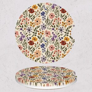 May include: Two car coasters with a floral pattern. The coasters feature a cream background with a repeating pattern of colorful flowers in shades of red, pink, yellow, purple, and blue, with green leaves.