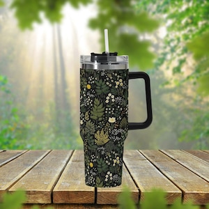 May include: A black stainless steel travel mug with a floral pattern and a black handle. The mug has a clear lid with a straw.