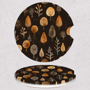 May include: Two car coasters with a forest design. The coasters are round with a dark brown background and feature a pattern of trees in shades of brown, tan, and white. One coaster has a notch for a car cup holder.