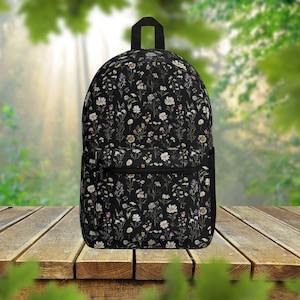 May include: A black backpack with a floral pattern featuring small white and pink flowers on a black background. The backpack has a zipped front pocket.