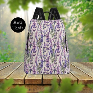 May include: A lavender floral print backpack with black straps and zipper pulls. The backpack has the words "Anti Theft" printed on the front.