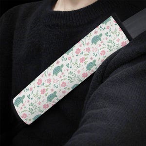 May include: White car seatbelt cover with a pattern of green turtles and pink flowers.