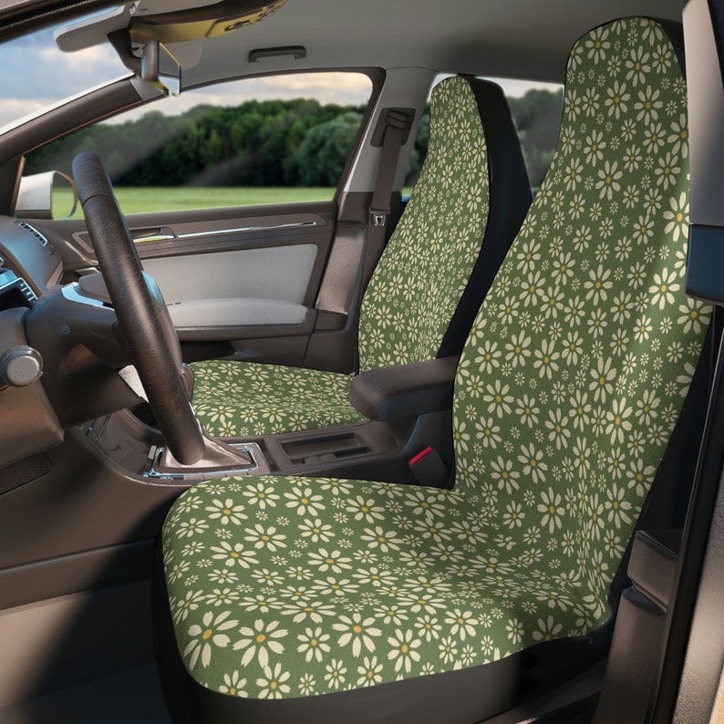 May include: Two green car seat covers with a white daisy pattern. The covers are installed in the front seats of a car.