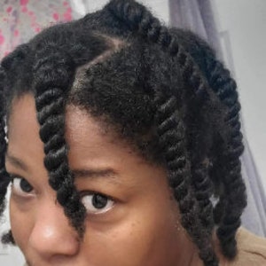 May include: A close-up of a person with dark brown hair styled in twists. The person is wearing a light brown shirt.