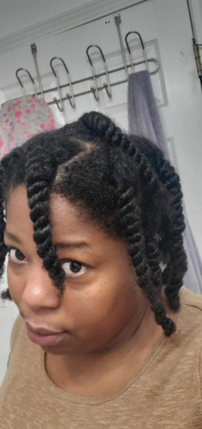 May include: A close-up of a person with dark brown hair styled in twists. The person is wearing a light brown shirt.