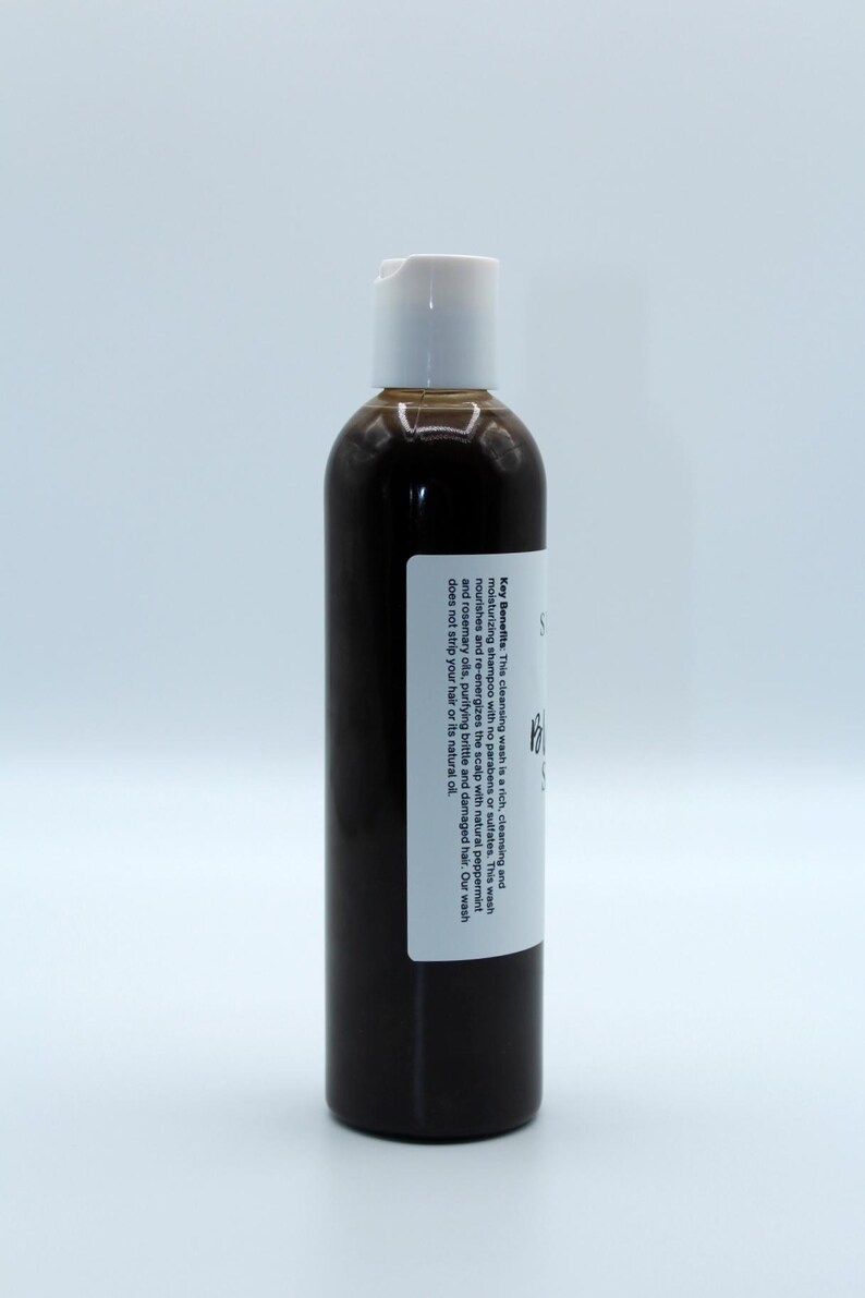 May include: A brown bottle of hair wash with a white label. The label reads "Key Benefits: This cleansing wash is a rich, cleansing and moisturising shampoo with no parabens or sulphates. This wash nourishes and re-energises the scalp with natural peppermint and rosemary oils, purifying brittle and damaged hair. Our wash does not strip your hair or its natural oil."