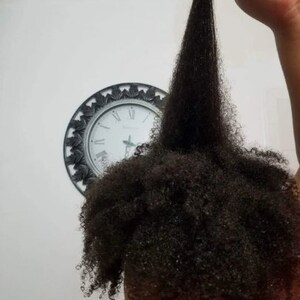 May include: A person with long, dark, curly hair. The hair is pulled up and held in one hand, showing the length of the hair.