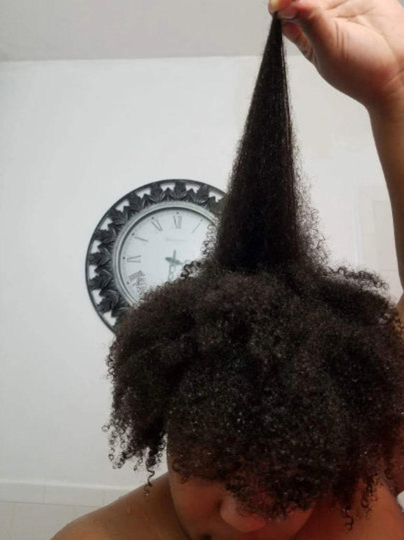 May include: A person with long, dark, curly hair. The hair is pulled up and held in one hand, showing the length of the hair.