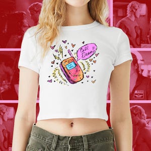 May include: White crop top with a colorful illustration of a retro cell phone. The phone is pink and orange with the text "from allie" on the screen. A speech bubble says "Call Dean!!" surrounded by hearts and lightning bolts.