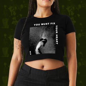 Könnte beinhalten: Schwarzes Crop-Top mit dem Text "YOU MUST FIX YOUR HEART" und einer schwarz-weißen Grafik einer Hand, die ein Herz mit Flammen hält. Die Grafik befindet sich in einem Quadrat mit einem kreisförmigen Muster. Die Buchstaben "MCR" stehen unten.