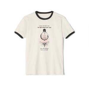 Könnte beinhalten: Ein weißes T-Shirt mit einem schwarzen Ringelkragen. Das Shirt zeigt eine Schwarzweißillustration einer Glühbirne mit einer umherfliegenden Motte. Der Text "never let them take the light behind your eyes you will always burn as bright" ist auf dem Shirt aufgedruckt.