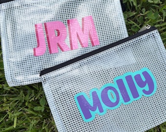 May include: Two rectangular clear pouches with a white grid pattern and black zippers. One pouch features the pink letters JRM, while the other pouch displays the name Molly in purple letters with a bright blue outline on the front surface.