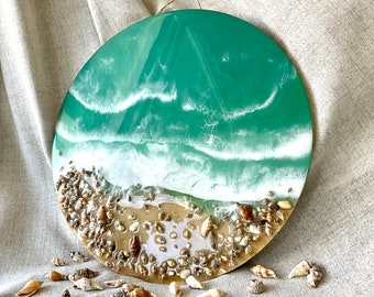 Könnte beinhalten: Ein rundes Harz-Kunstwerk, das einen grünen Ozean mit weißen Wellen darstellt, die an einem Sandstrand brechen. Der Strand ist mit kleinen Muscheln verziert.