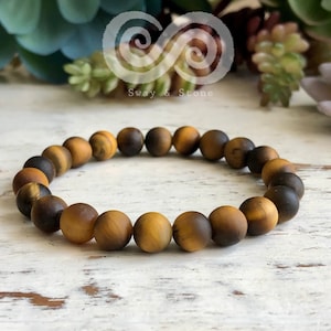 May include: A brown and gold tiger's eye beaded bracelet. The bracelet is made of round beads and has a simple design.
