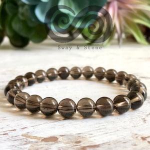 May include: A dark brown smoky quartz beaded bracelet. The bracelet is made of round beads and is strung on elastic.