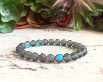 Puede incluir: Un brazalete gris de cuentas con cuentas iridiscentes. Las cuentas tienen un acabado mate y brillan con tonos azules y verdes.