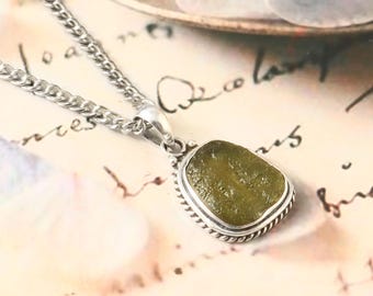 May include: A silver chain necklace with a green sea glass pendant set in a silver bezel. The pendant has a rope-like border.