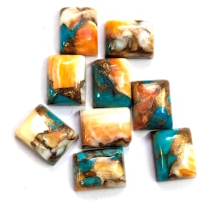 Puede incluir: Una colección de cabujones de piedras preciosas rectangulares. Las piedras presentan una mezcla de colores, incluyendo turquesa, naranja, blanco y dorado. Cada piedra tiene un patrón único sobre un fondo blanco. Estas piedras son adecuadas para la fabricación de joyas.