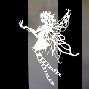 Peut inclure: Découpe en papier blanc d'une fée avec des ailes et un papillon dans sa main. La fée est suspendue au plafond.