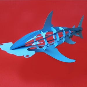 Könnte beinhalten: Ein blaues Papiermodell eines Hammerhais mit einem detaillierten, komplizierten Design. Der Hai ist in Schwimmposition mit dem Kopf nach oben geneigt.