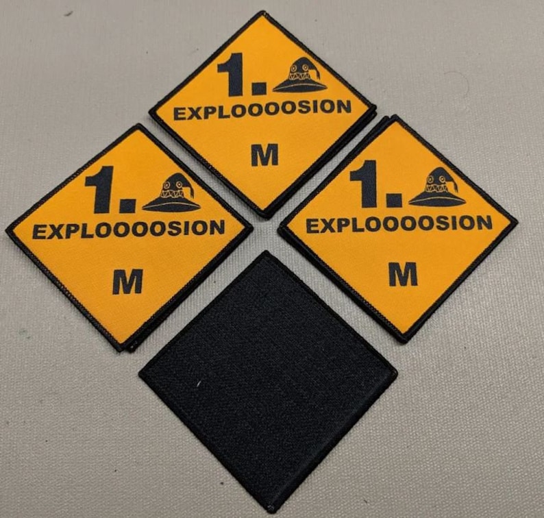May include: Three yellow diamond-shaped patches with black borders and the text "1. EXPLOOOOOSION M" and a black cartoon image of a wizard's hat. A black diamond-shaped patch is in the center.