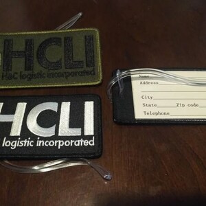 May include: Two black and green luggage tags with the text "HCLI H&C logistic incorporated" and a white luggage tag with the text "HCLI H&C logistic incorporated" and a blank white label with fields for name, address, city, state, zip code, and telephone.