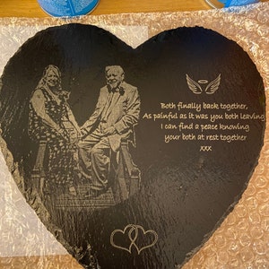 Puede incluir: Una pizarra negra en forma de corazón grabada con una foto de una pareja y un mensaje que dice: "Both finally back together, As painful as it was you both leaving I can find a peace knowing your both at rest together XXX".