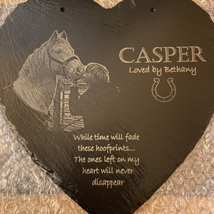 Op de afbeelding: Zwarte hartvormige leiste gegraveerd met een paard en ruiter, de naam "CASPER" en de tekst "Loved by Bethany". De leisteen bevat ook een hoefijzer en het citaat "While time will fade these hoofprints... The ones left on my heart will never disappear."