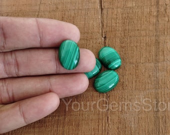 Puede incluir: Cuatro piedras preciosas ovaladas de malaquita verde con vetas blancas. Las piedras están dispuestas en un racimo en una mano.