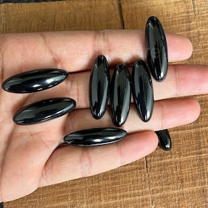 May include: Eight black oval-shaped stones, likely obsidian, are arranged on a hand. The stones are smooth and polished.