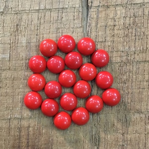 Könnte beinhalten: Eine Gruppe von 20 leuchtend roten runden Cabochon-Edelsteinen, die in einem sechseckigen Muster auf einer Holzoberfläche angeordnet sind.