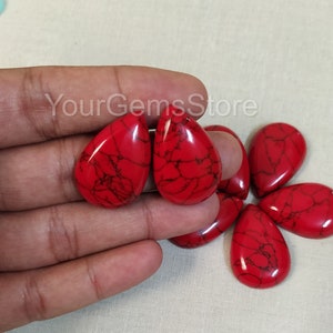 May include: A collection of red teardrop-shaped cabochons with a marbled pattern. The cabochons are made of red jasper and are ideal for jewellery making.