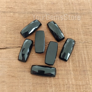 Peut inclure: Sept pierres précieuses rectangulaires facettées noires sur une surface en bois. Les pierres précieuses sont toutes de la même taille et de la même forme.