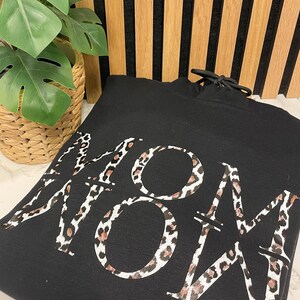 Könnte beinhalten: Schwarzer Kapuzenpullover mit einem Leopardenmuster "MOM".