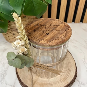 Könnte beinhalten: Ein Glasgefäß mit einem Holzdeckel, verziert mit einem Herz und dem Text "Alles Liebe zu deiner Konfirmation" in einem Kranz. Das Gefäß ist mit Schnur gebunden und hat ein kleines Schild mit der Aufschrift "Von Herzen". Das Gefäß steht auf einer Holzscheibe.