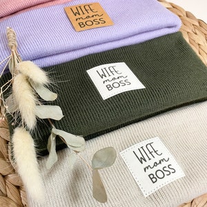 Pode incluir: Quatro gorros de malha em cores diferentes, empilhados uns sobre os outros. Cada gorro tem um remendo quadrado branco com o texto "Wife Mom Boss" em preto.