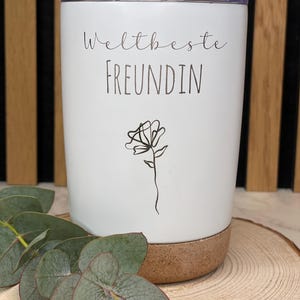 Op de afbeelding: Witte geïsoleerde beker met een kurken bodem. De beker heeft de tekst "Weltbeste Freundin" en een eenvoudige lijntekening van een bloem.