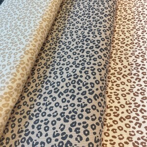 May include: Three rolls of fabric with a leopard print pattern. The fabric colors are beige, gray, and brown. The leopard spots are dark gray and brown. The fabric is ribbed.