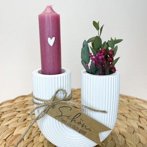 Könnte beinhalten: Weißer Kerzenhalter aus Keramik in U-Form mit einer rosa Kerze und einem kleinen Strauß aus Grün und rosa Beeren. Der Halter hat ein braunes Etikett mit der Aufschrift "Schön, dass es dich gibt!"