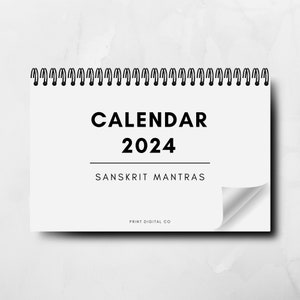 Peut inclure: Un calendrier blanc avec une reliure spirale noire. Le calendrier est intitulé "CALENDAR 2024" et porte les mots "SANSKRIT MANTRAS" sous le titre. Le bas du calendrier indique "PRINT DIGITAL CO."