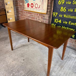 May include: A rectangular wooden dining table with a smooth, dark brown finish and four tapered legs. The table features a visible seam across the centre, indicating an extendable design, with a flat, polished surface and clean, straight edges.