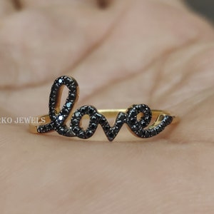May include: A gold ring with black diamonds spelling out the word "love".
