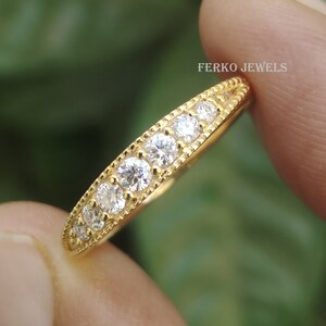 May include: A gold band ring with a row of clear round stones. The ring is on a finger and the text "FERKO JEWELS" is visible in the background.
