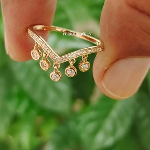 Op de afbeelding: Een goudkleurige ring met een V-vormig ontwerp. De ring is versierd met kleine, hangende cirkelvormige bedels, elk met een heldere edelsteen. De bovenkant van de V is bekleed met kleine, heldere edelstenen. De tekst "FERKO JEWELS" is zichtbaar.