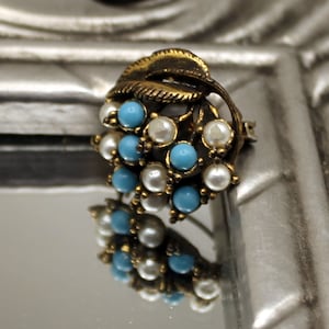 May include: A gold-toned brooch with a leaf design and blue and white faux pearls.