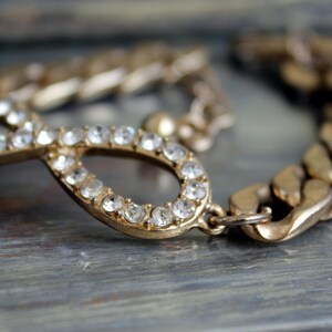 May include: A gold infinity symbol charm bracelet with clear rhinestones. The bracelet has a chunky gold chain link design.