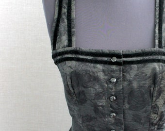 Puede incluir: Un vestido gris con estampado floral, exhibido en un maniquí. El vestido presenta un escote cuadrado, una botonadura frontal y ribetes de terciopelo negro en los tirantes y el escote. El vestido es de estilo vintage.